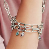 Silver chain bracelet with charms on a wrist against a pink background