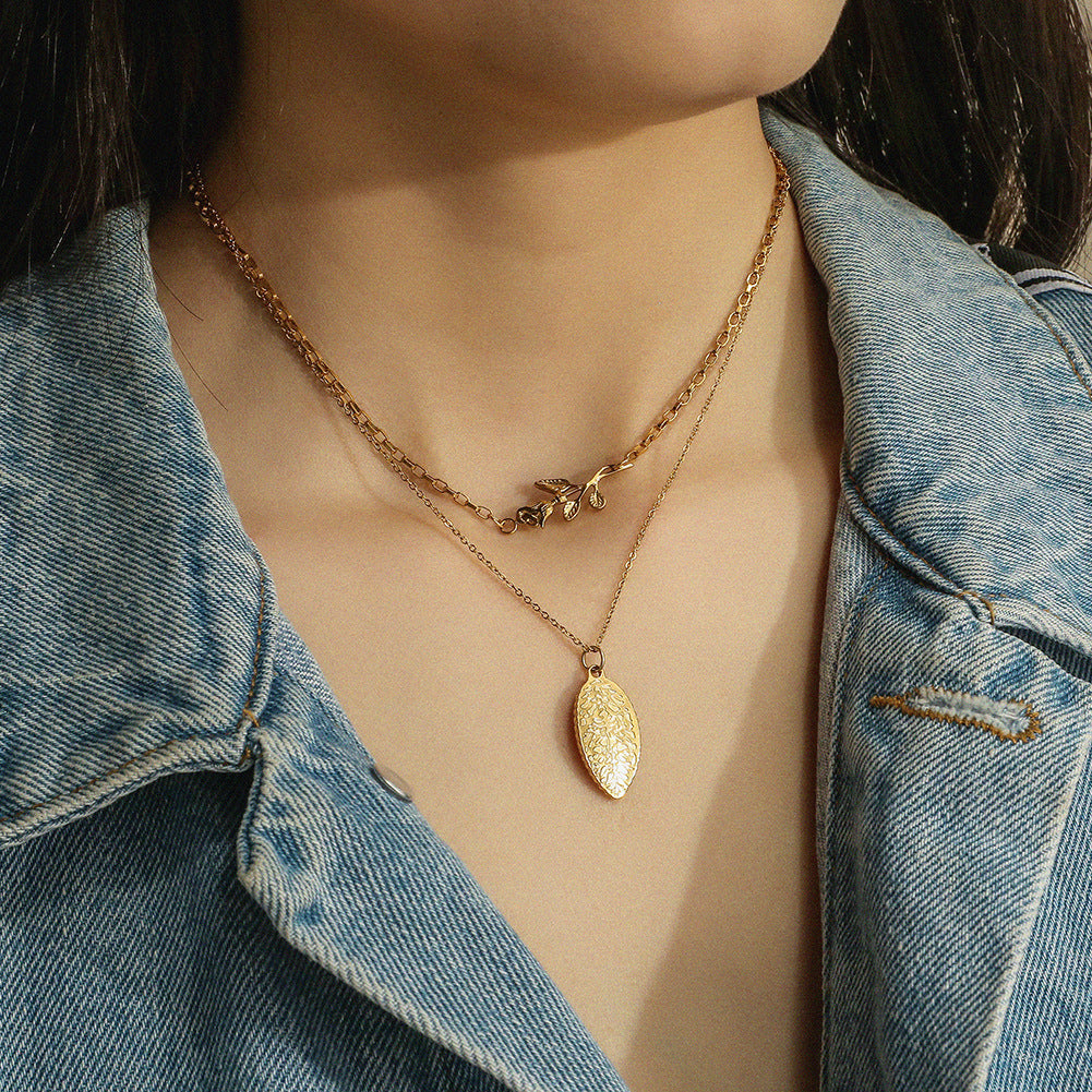 Gold necklace with a leaf pendant worn by a person in a denim jacket.