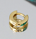 Gold earring with green gemstone on a reflective surface