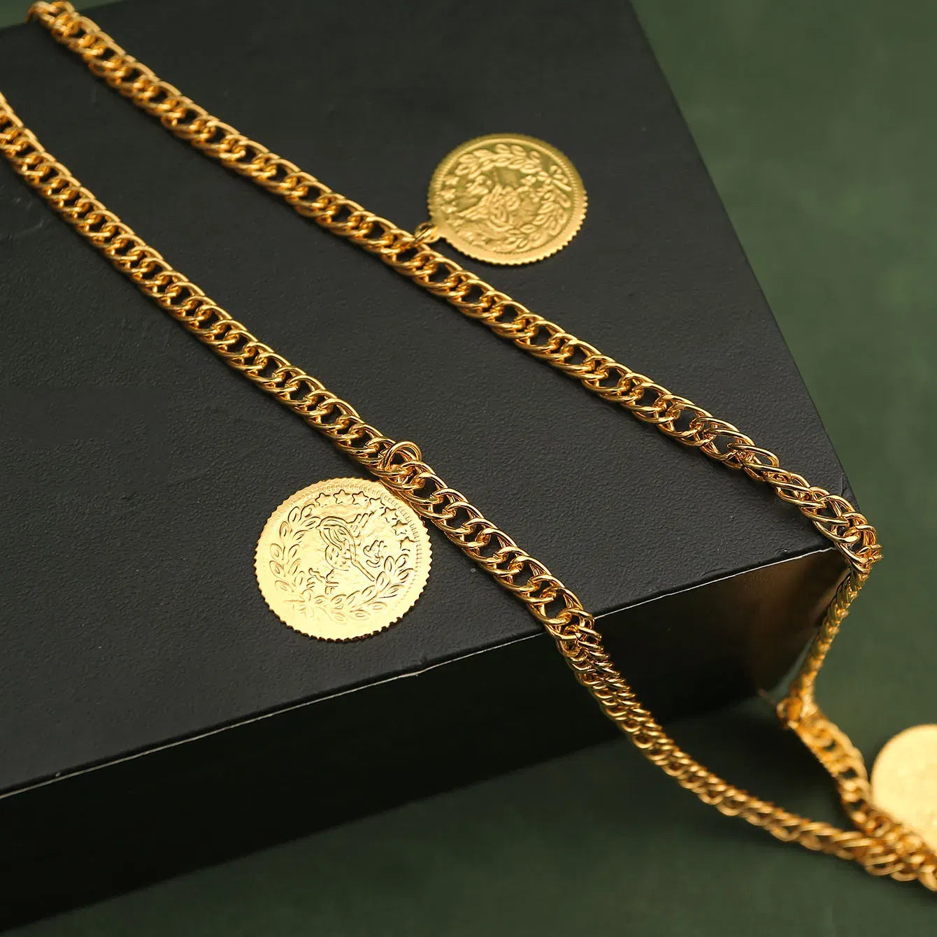 Gold chain and coins on a black surface with a green background